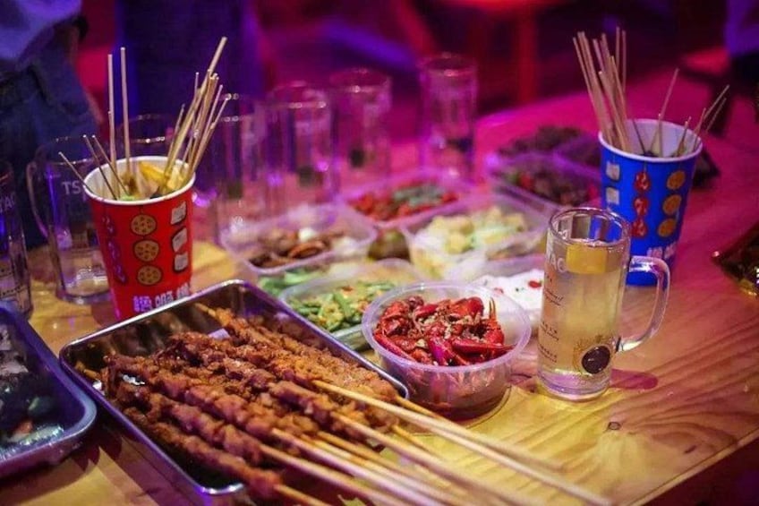 A table with various food items, including skewers, a drink, and a cup with chopsticks. 4