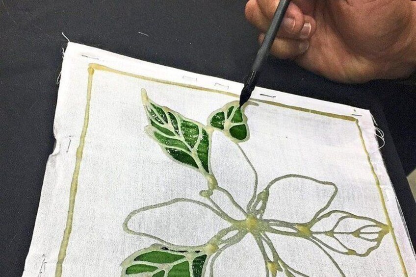 A hand painting a floral design on fabric. 1