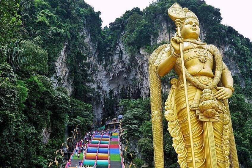 A large golden statue of a deity with a staff, set against a cliffside with a colorful stairway leading up to it. 2