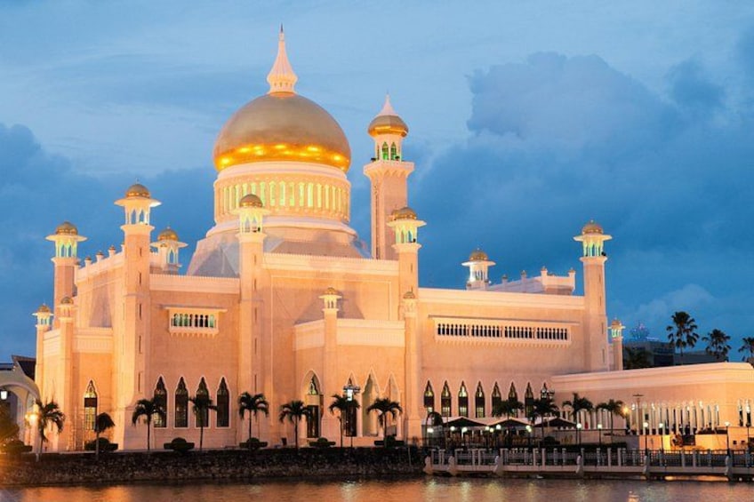 A large, illuminated mosque with multiple domes and minarets, surrounded by palm trees and a body of water. 5