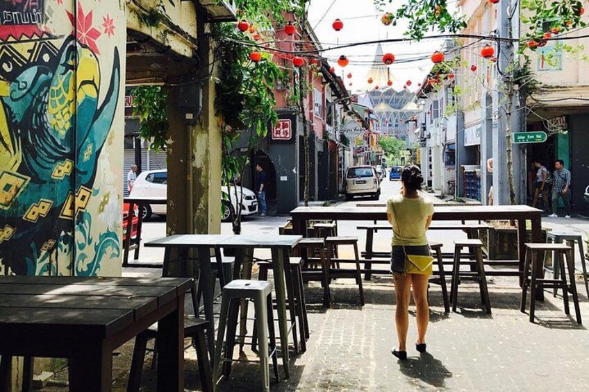 A street with tables and chairs, a mural, and hanging decorations. 2