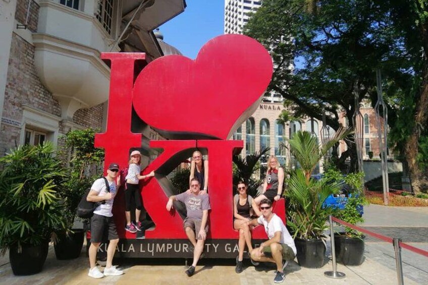 A group of people posing in front of a large red heart-shaped sign with the text 'I ❤️ KL' and 'KUALA LUMPUR CITY GALL.' 5