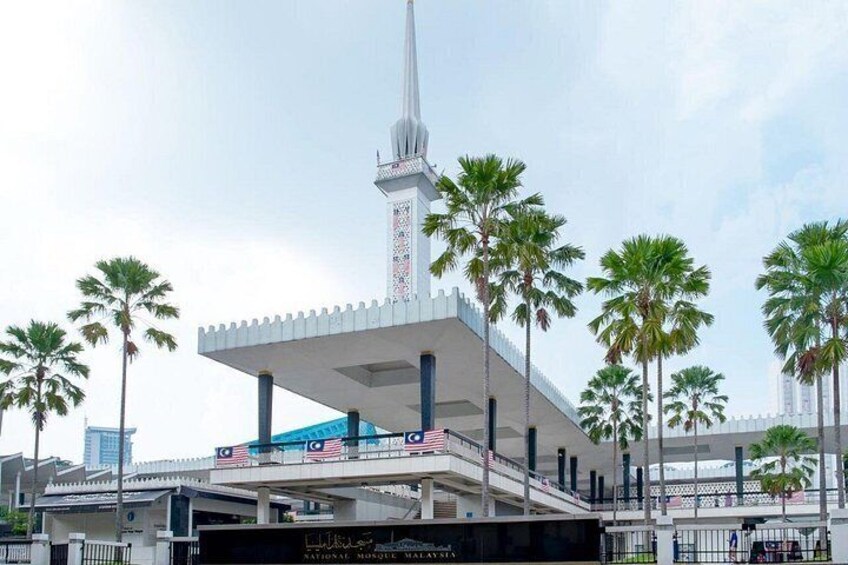 A modern building with a tall spire, palm trees, and a bridge with flags. 4