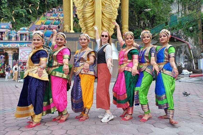 A group of people in colorful traditional attire standing in a public square with a large golden statue in the background. 5
