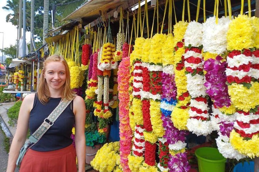 A person standing in front of a wall of colorful flower garlands. 2