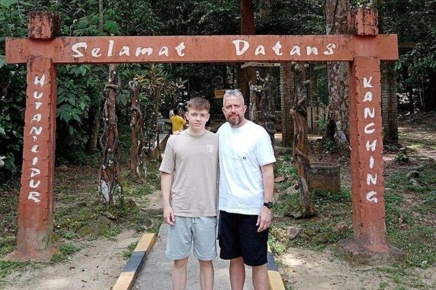 Two people standing under a wooden archway with inscriptions. 2