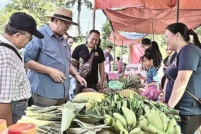 People at a market stall with bananas and other produce. 5