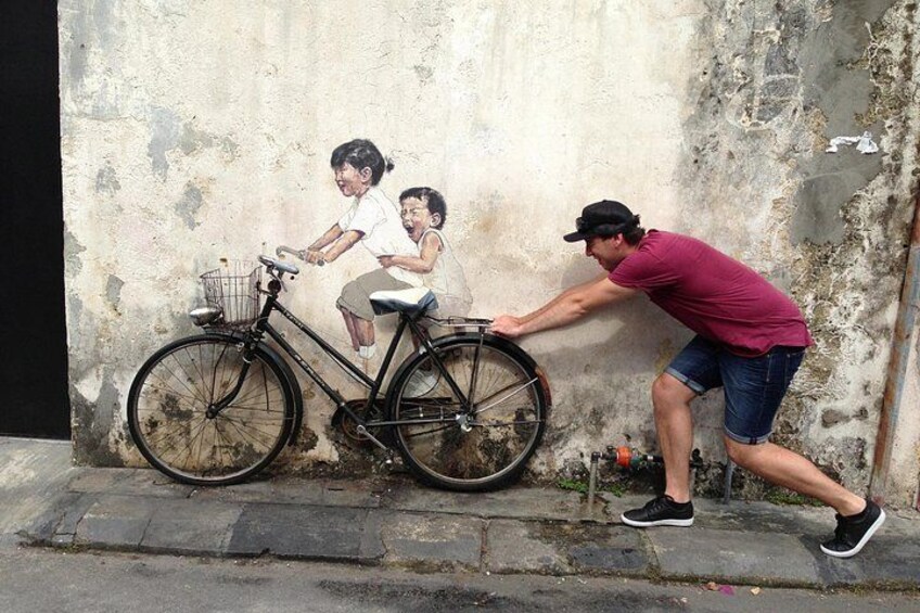 A mural of a child on a bicycle, a man pushing the bike, and a wall with peeling paint. 5