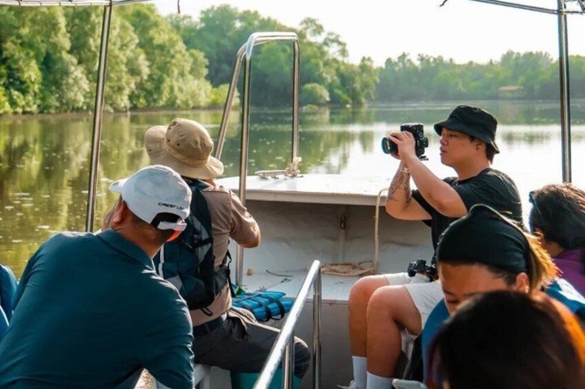A group of people on a boat, some taking photos, with a calm lake and greenery in the background. 1