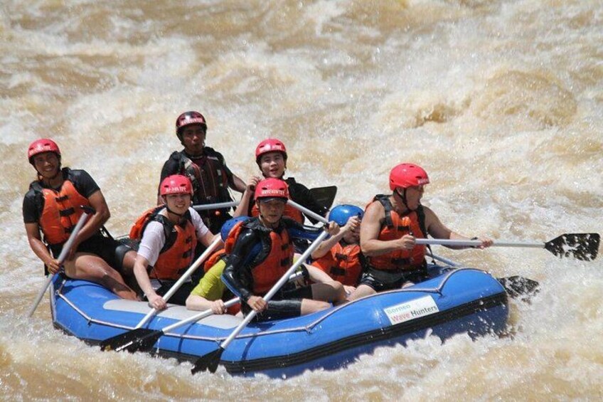 A group of people in a blue raft navigating a river with white water rapids. 2