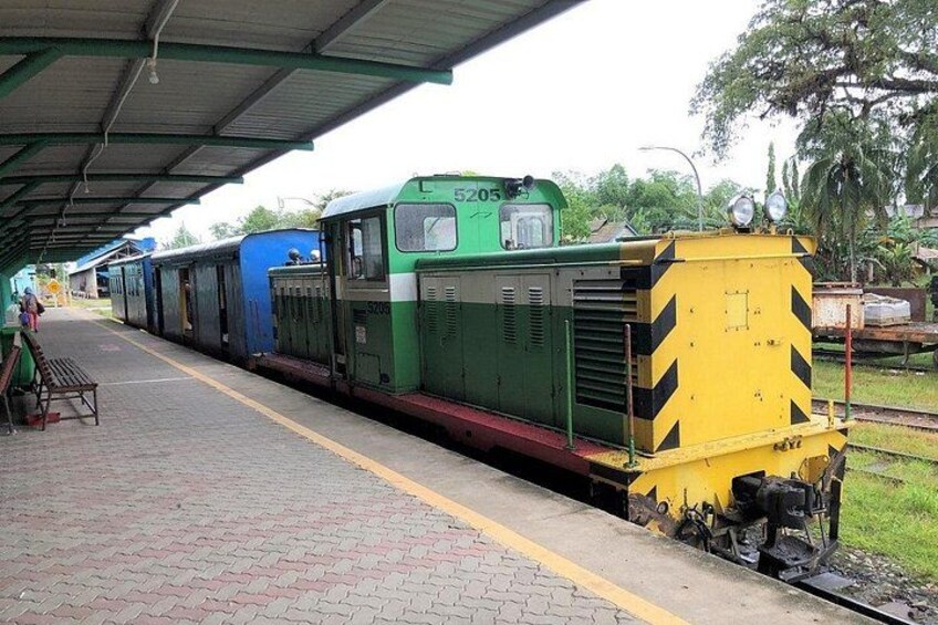 A green and yellow train at a station platform with a covered roof and a bench. 5