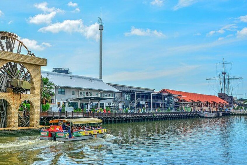 A river with a water wheel, a tall tower, and a boat with people. 2