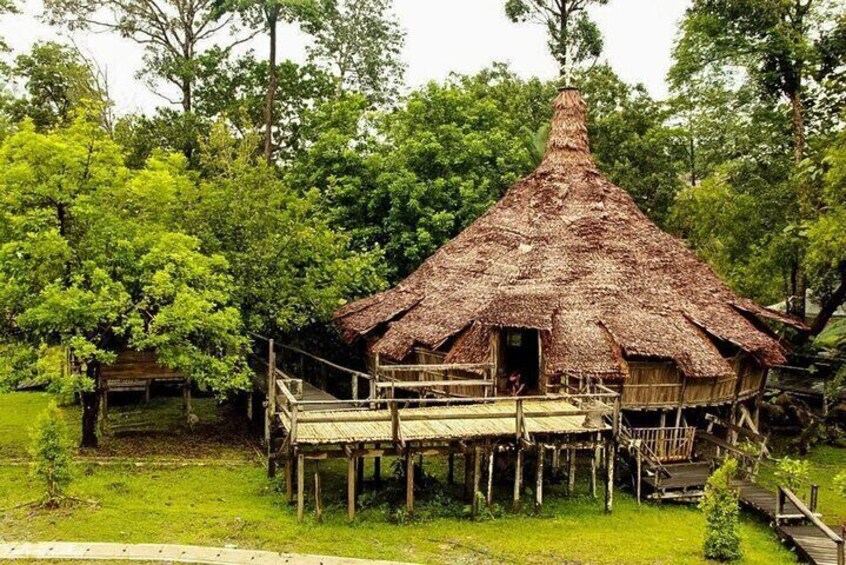 A thatched-roof hut with a wooden deck, surrounded by lush greenery. 4