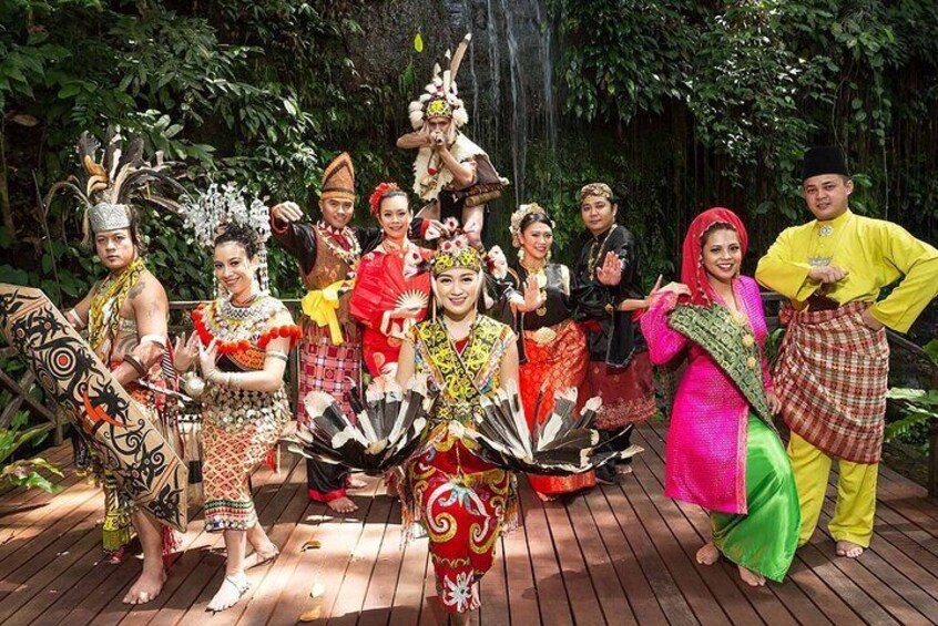A group of people in traditional costumes performing a dance on a wooden deck with a waterfall in the background. 1