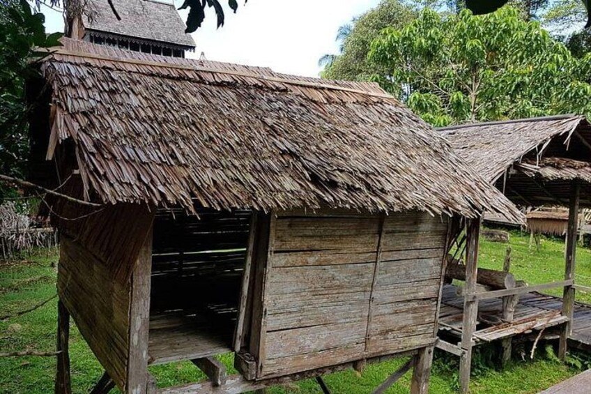 A rustic wooden structure with a thatched roof, surrounded by greenery. 4