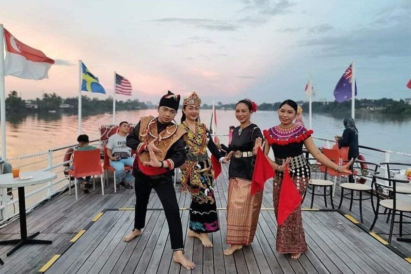 A wooden deck with people in traditional attire, flags, and a calm body of water in the background. 1