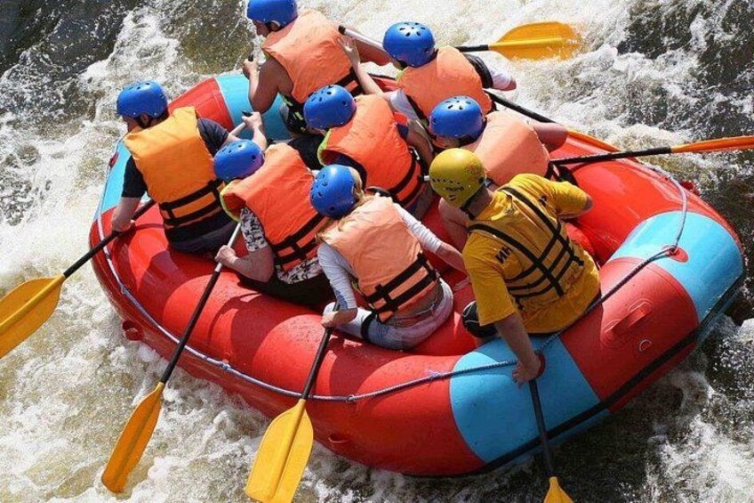 A group of people in a red and blue inflatable raft on a river, paddling with yellow paddles. 3
