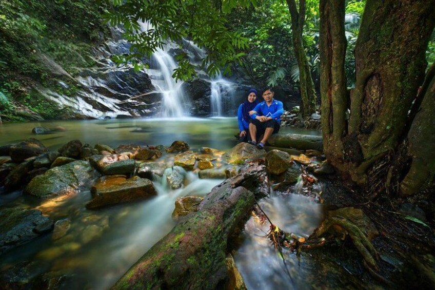A waterfall, rocks, and two people sitting by the water. 2