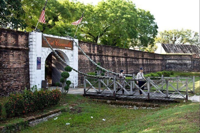 A historic fort entrance with a brick wall, American flags, and a wooden bridge. 2