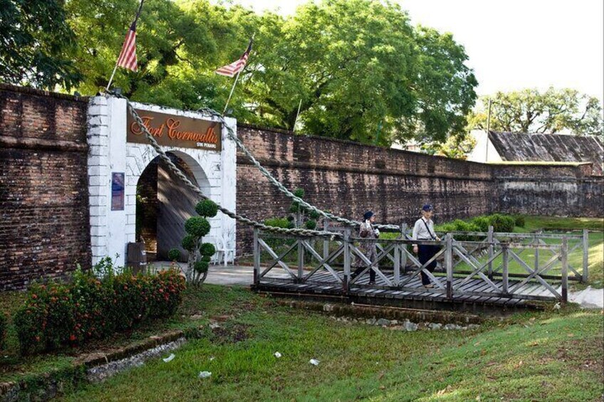 A historic fort entrance with a brick wall, American flags, and a wooden bridge. 2