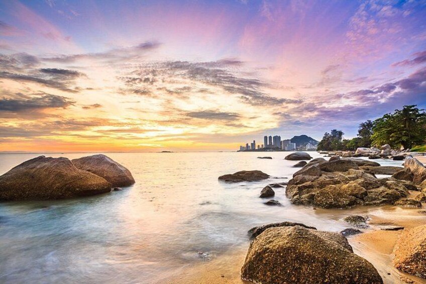 A coastal landscape with large rocks, calm water, and a city skyline in the distance during sunset. 4