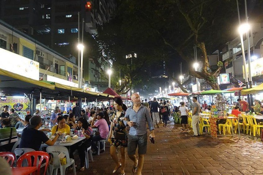 A bustling outdoor market at night with people walking and dining. 2