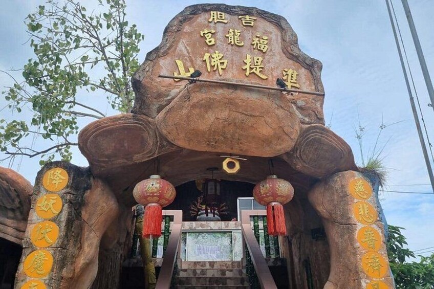 A traditional Chinese temple entrance with a large rock structure, red lanterns, and Chinese characters. 4