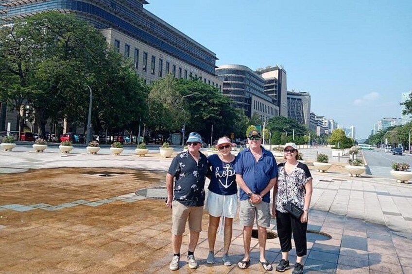 Un groupe de personnes se tient sur une place publique, avec des bâtiments en arrière-plan. 3