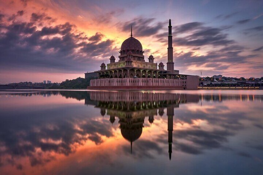 A mosque with a large dome and a minaret, reflected in calm water, with a sunset sky. 5