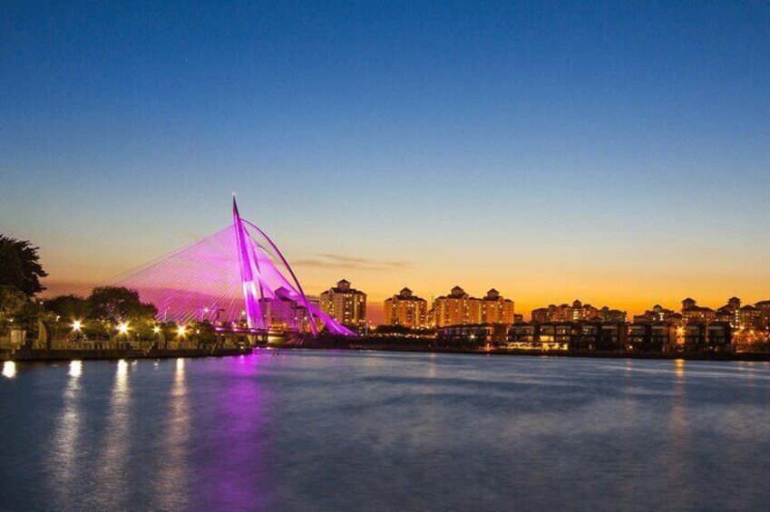 A lit bridge at dusk with a city skyline in the background. 2