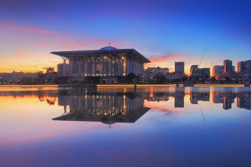 A modern building with a dome, reflecting in a calm body of water, with a city skyline in the background. 3