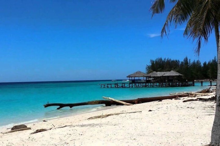 A beach with clear turquoise water, white sand, and a wooden structure on stilts in the background. 2