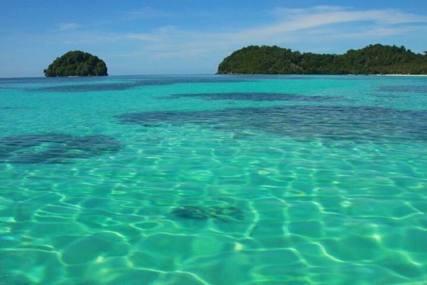 Clear turquoise water, a small island, and a larger landmass with dense greenery. 3