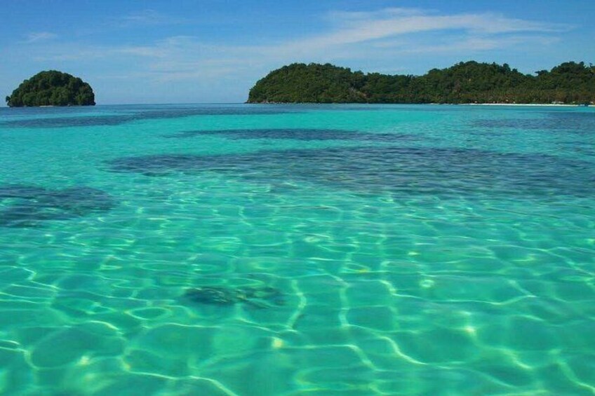 Clear turquoise water, a small island, and a distant landmass with dense greenery. 2