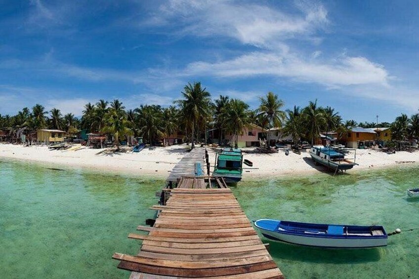A wooden pier leading to a beach with clear turquoise water, palm trees, and small boats. 3