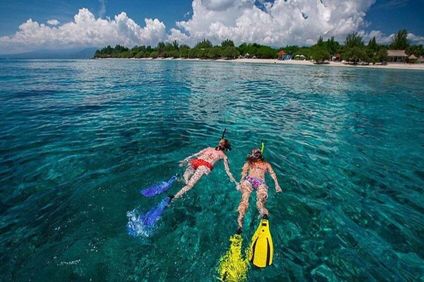 Two people snorkeling in clear blue water with a tropical island in the background. 2