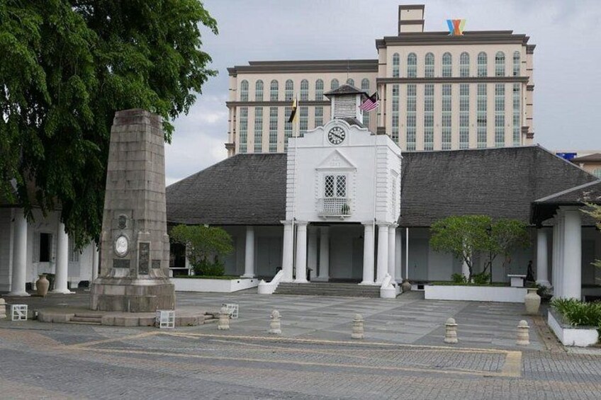 A building with a white facade, a stone monument, and a flag. 4