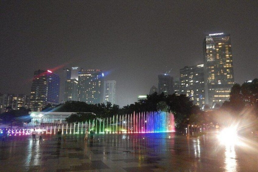 A cityscape at night with illuminated buildings and a fountain display. 3