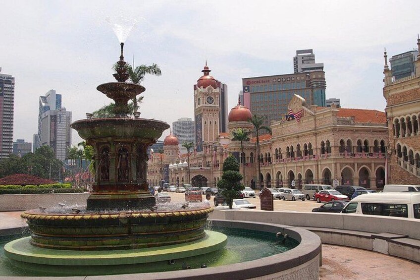 A fountain with water jets, a large building with a clock tower, and a modern skyscraper in the background. 4