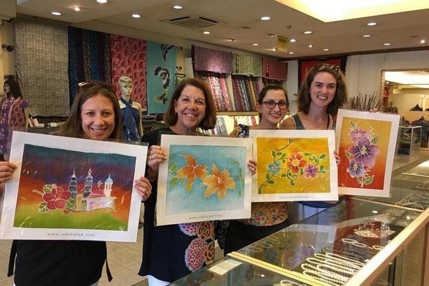 Four people holding up paintings in a store with various fabrics and mannequins in the background. 5