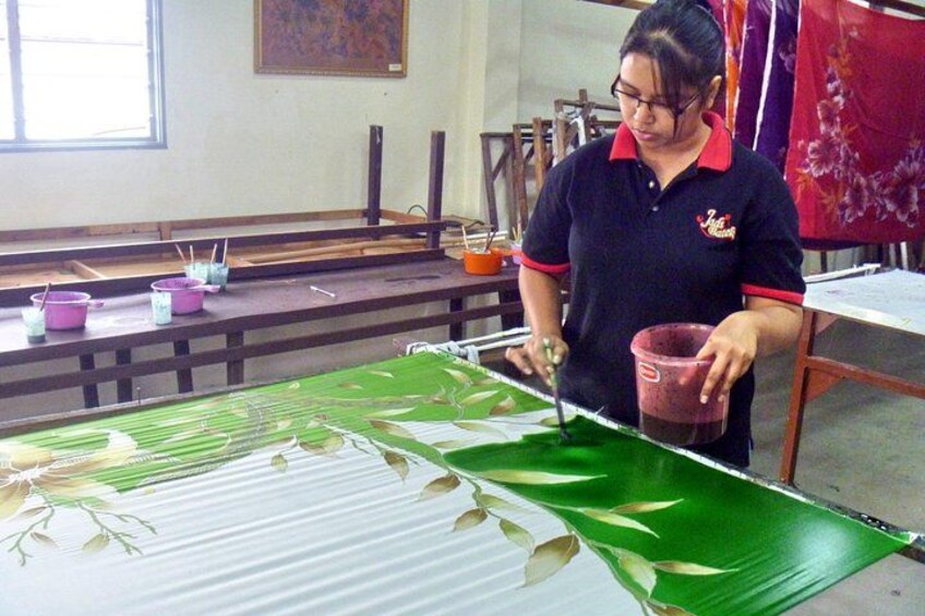 A person working with a large green leaf-like material, possibly for crafting or art, in a room with wooden benches and tables. 4