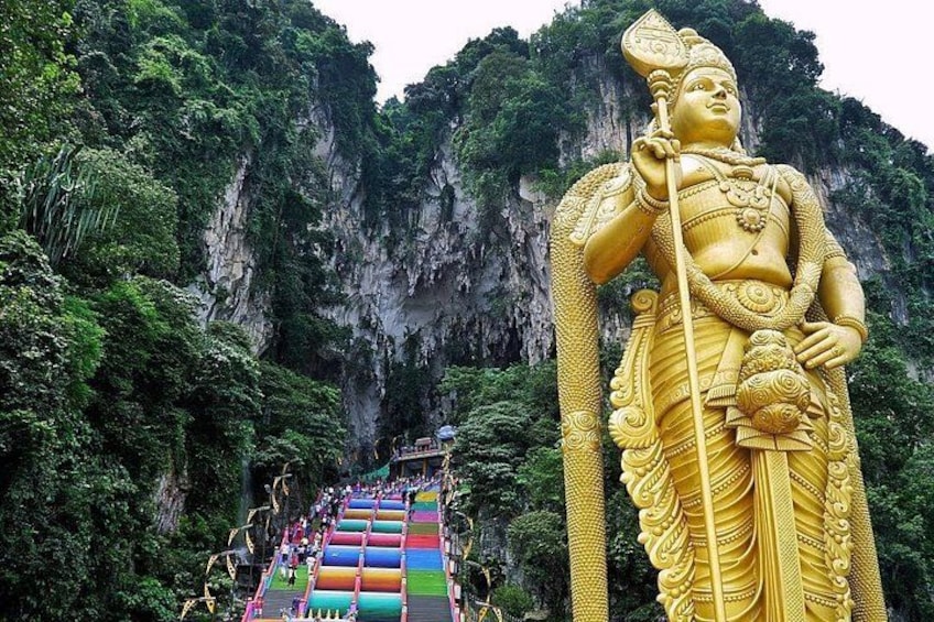 A large golden statue of a deity with a staff, set against a cliffside with a colorful stairway leading up to it. 2