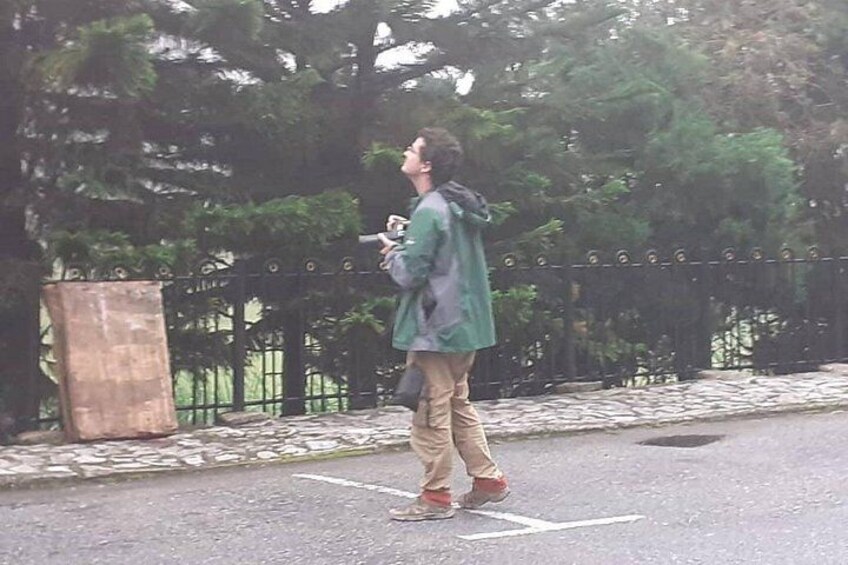 A person walking on a paved path with a metal fence and trees in the background. 3