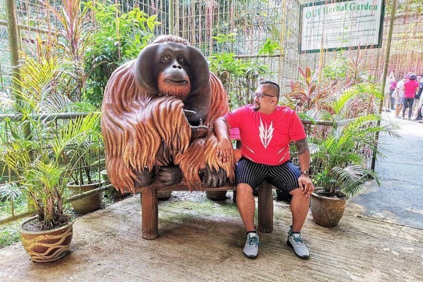 A man sitting next to a large orangutan statue in a garden with potted plants. 2