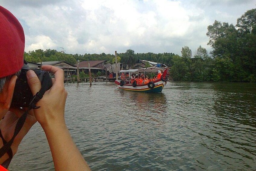 A person taking a photo of a boat with passengers, a dock, and trees in the background. 4
