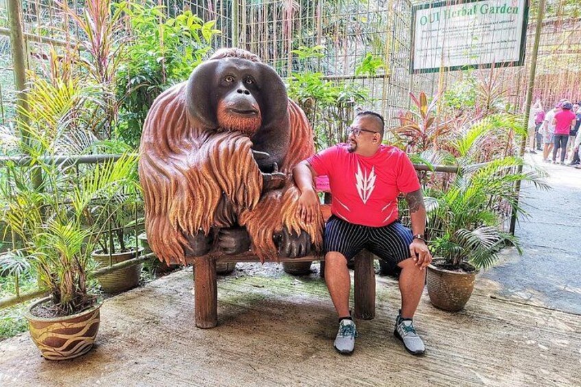 A man sitting next to a large orangutan statue in a garden with potted plants. 2