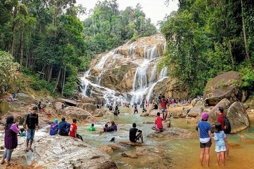 A waterfall surrounded by rocks and trees with people sitting and standing around. 5