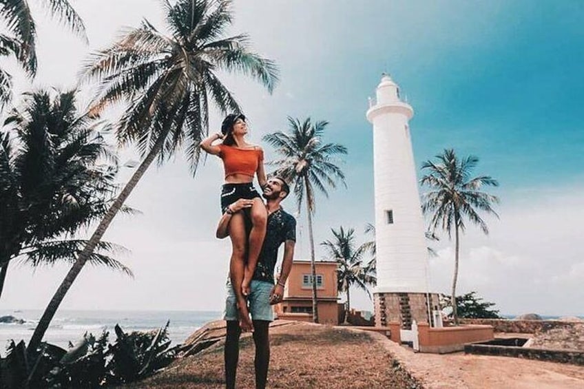 A couple on a beach with a lighthouse and palm trees. 1