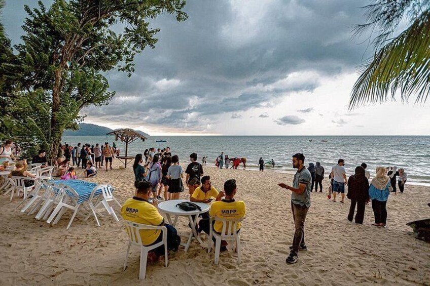 A beach with people, chairs, and tables under a cloudy sky. 2