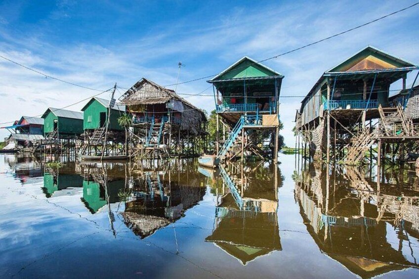 Floating houses on water with reflections, wooden stilts, and a clear sky. 5